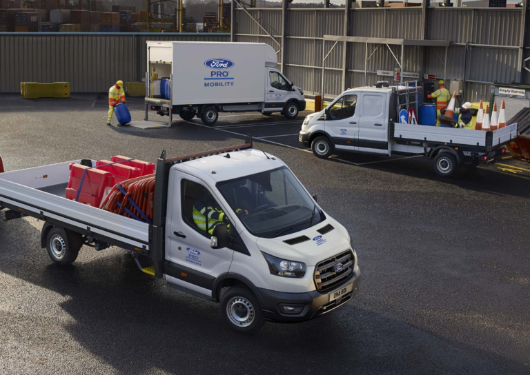 Drei verschiedene Ford Transit, die auf einer Baustelle an der Straße eingesetzt werden. Arbeiter in Arbeitskleidung und Sicherheitswesten sind damit beschäftigt, Straßenreparaturen durchzuführen, während die Fahrzeuge als mobile Werkstätten und Transportmittel für Werkzeuge und Materialien dienen.